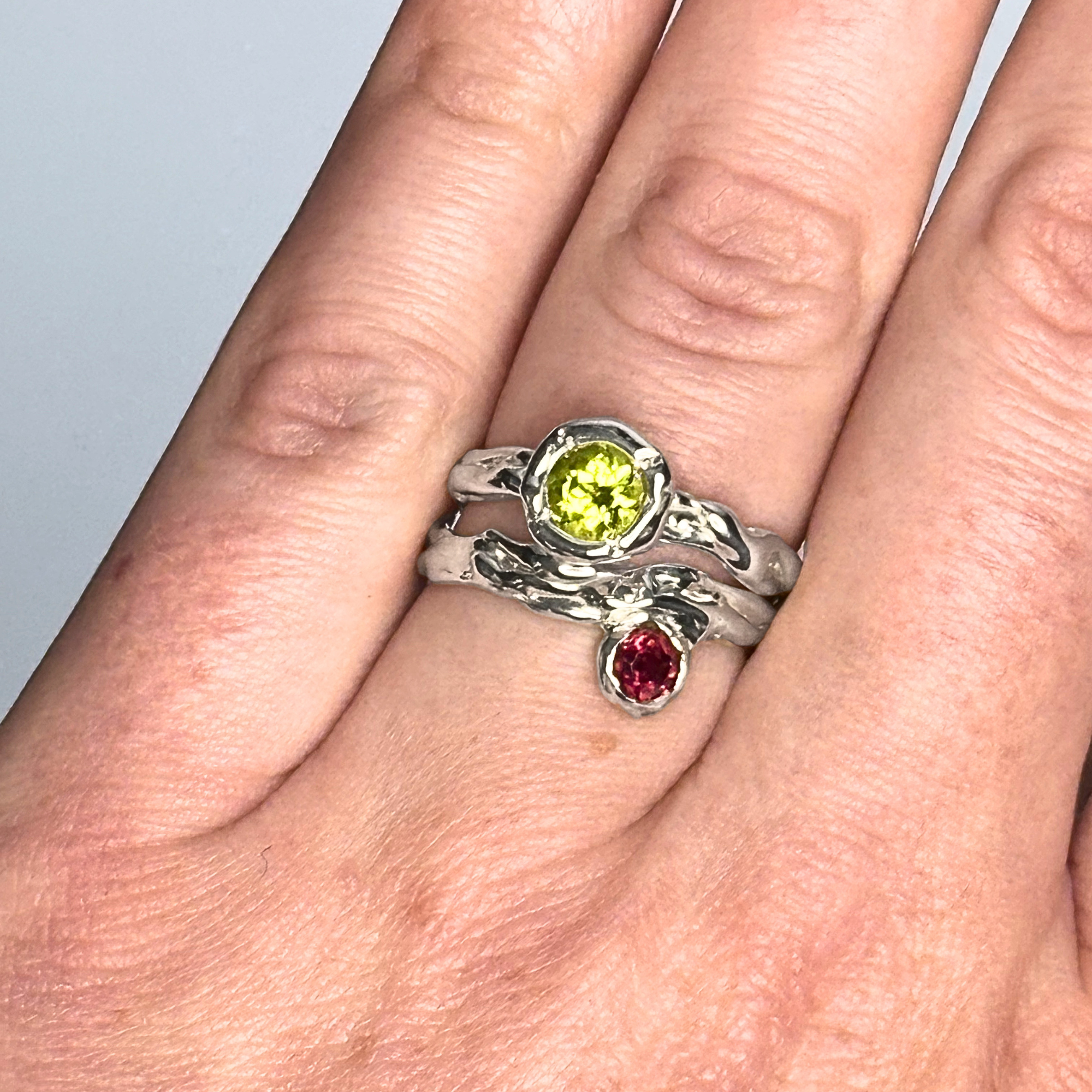 The Archive Series Rhodolite Garnet Solitaire and Peridot Solitaire worn as a bespoke, sovereign artifact, emphasizing the intentional asymmetrical silhouette and tactile master-goldsmithing quality of the piece on the hand.