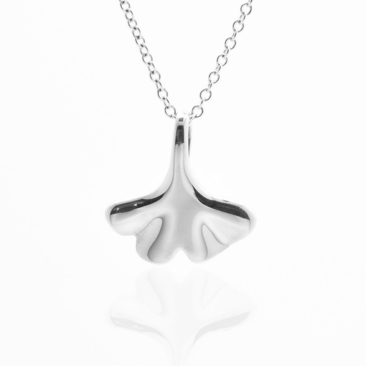 Angled studio shot with reflection of the Botanical Ginkgo Leaf Pendant 14mm petite in sterling silver, highlighting tactile volume and fine jewelry craftsmanship