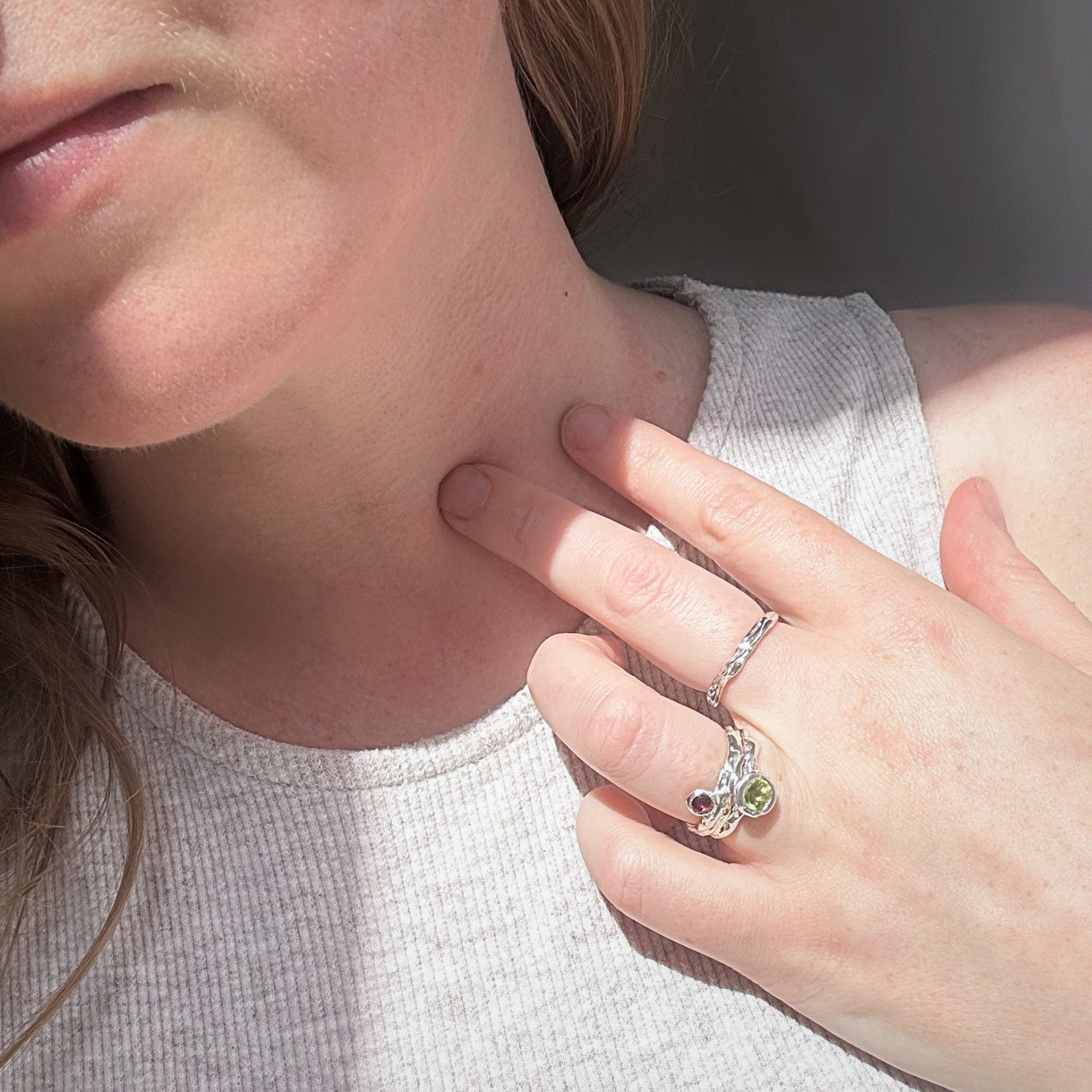Archive Series jewelry collection featuring a plain sculpted sterling silver band, a garnet solitaire, and a peridot solitaire, all showcasing bespoke master goldsmithing techniques.